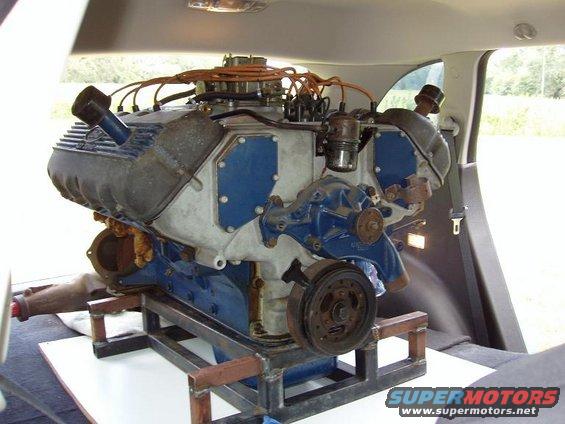 Engine on a metal stand inside a vehicle. Blue and silver engine with orange spark plug wires