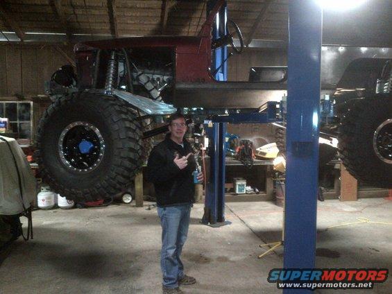 Modified Jeep body on a lift with oversized tires, a man stands beside it