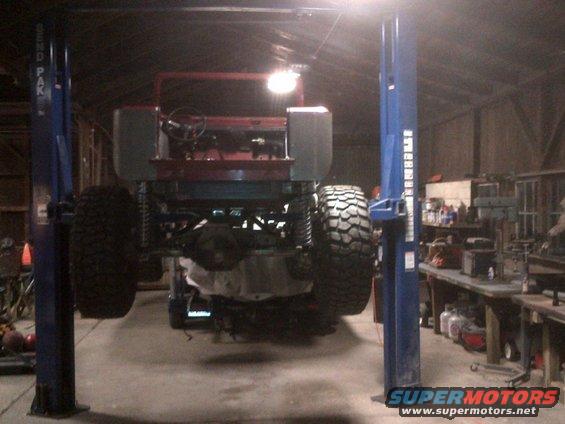 Red Jeep CJ-series on lift, rear view, large tires