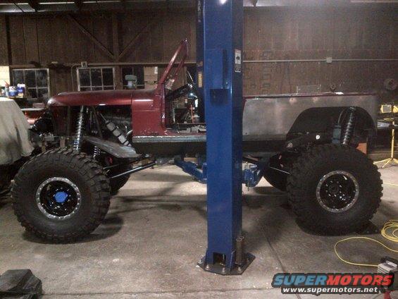 1985 Jeep CJ7 chassis undergoing modification, with large off-road tires and suspension components visible