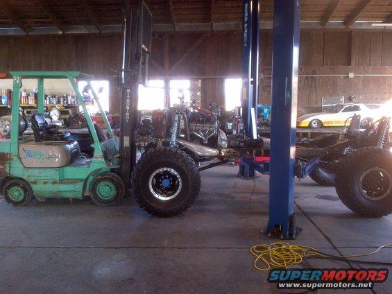 Jeep CJ frame with engine and large tires, a green forklift, and a drag car