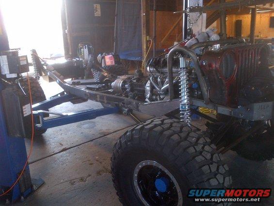 1985 Jeep CJ7 frame with engine and suspension components visible, in a garage