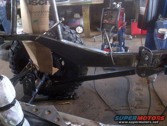 Jeep CJ frame with suspension components and a welding machine in background