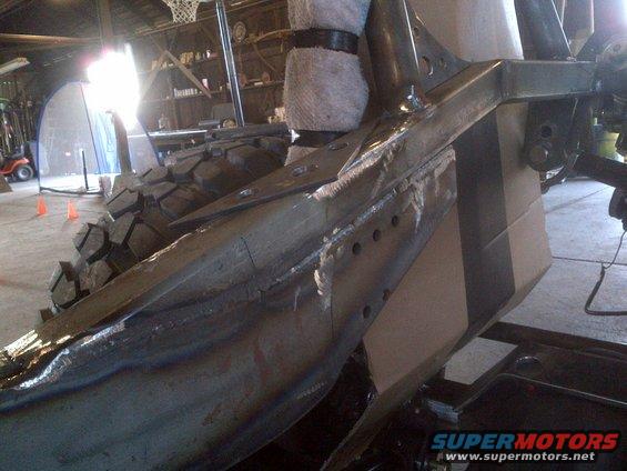 Jeep CJ frame with large tire, showing welded metal and suspension components in a workshop