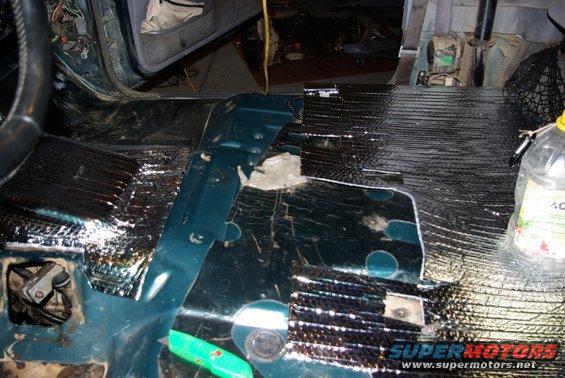 Car interior floor with sound deadening insulation installed, showing exposed metal and wiring