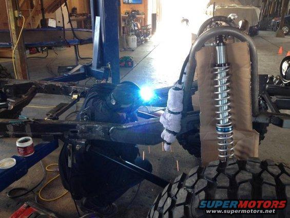 Welder working on vehicle frame with suspension components visible