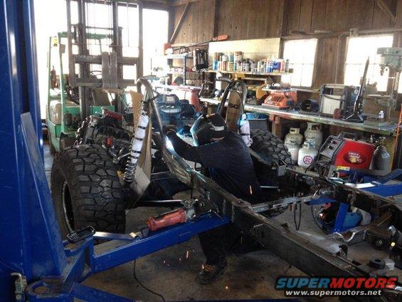 Welding a vehicle frame on a lift, with a forklift in the background