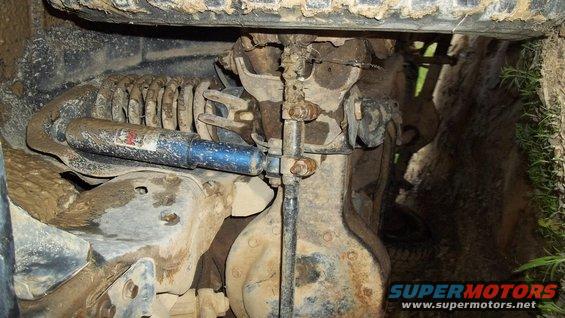 Undercarriage view of a suspension coil and blue shock absorber, covered in mud