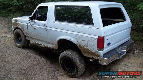 White 1990 Ford Bronco on a dirt trail, covered in mud