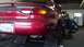 1996 Ford Taurus - A red 1996 Ford Taurus is being serviced in a garage, with a mechanic attending to the rear wheel.