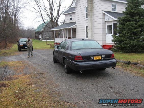 Dark gray 2003 Ford Crown Victoria sedan, rear view, parked on gravel driveway