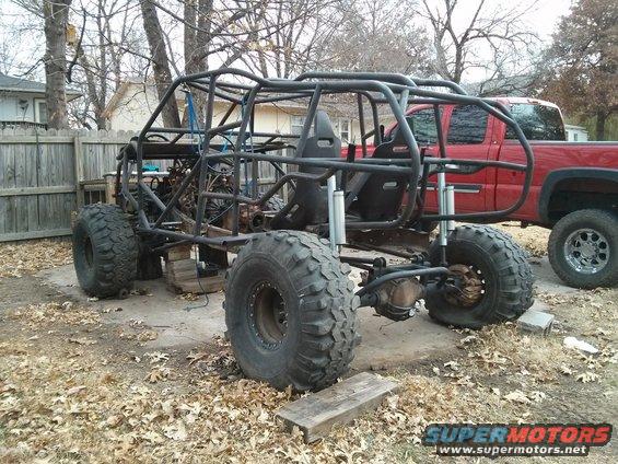 Custom buggy build with roll cage, large tires, and racing seats. Red pickup truck in background