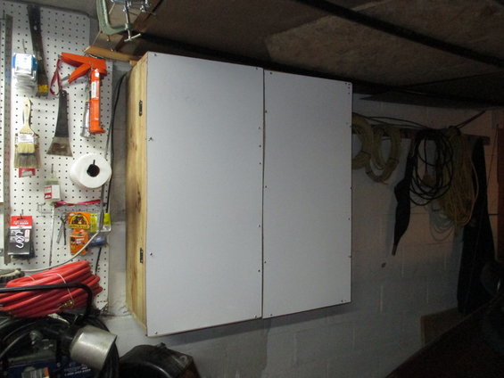 Cabinet with white doors and wooden sides mounted on a pegboard wall with tools