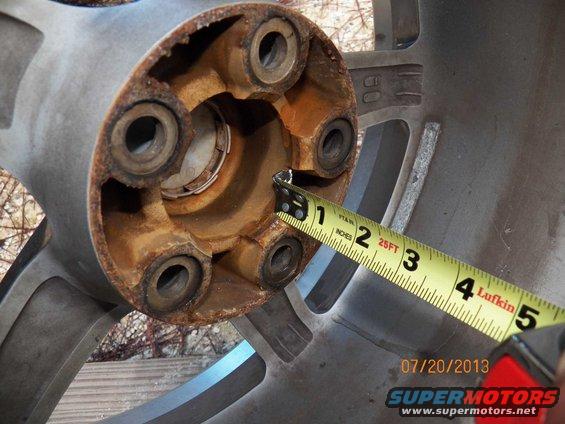 Close-up of a rusty wheel hub with a yellow measuring tape. Bolt holes are visible