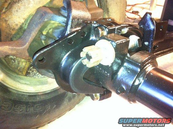 Close-up of a black painted vehicle axle assembly with a splined shaft and a white plastic cap