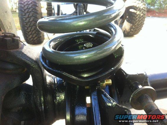 Close-up of a green suspension coil spring on a black axle assembly with a large tire in the background