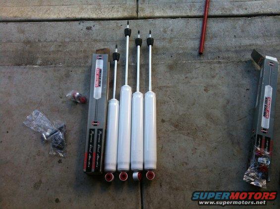 Four white shock absorbers with red ends and two boxes on a concrete surface