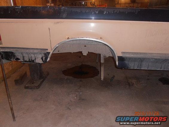 1988 Ford F-250 rear wheel well and bed side, showing rust and dirt. Truck is on jack stands