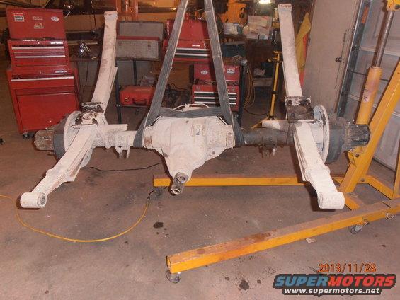 Front axle assembly suspended by straps, supported by a yellow engine hoist