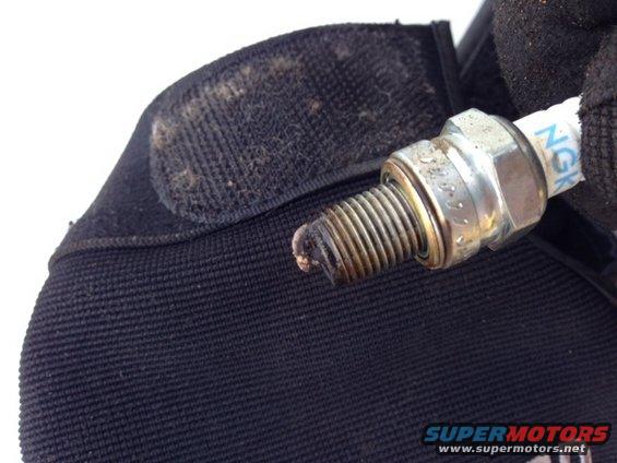 Spark plug with worn electrode held by gloved hand over black fabric
