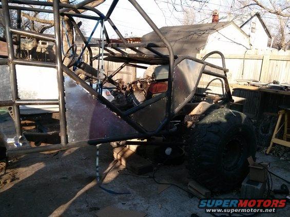 Custom buggy frame with large tires and exposed engine, in a yard