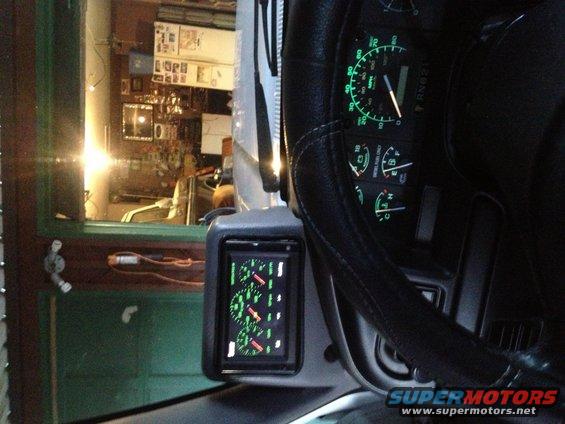 Vehicle interior showing a steering wheel, dashboard gauges, and an aftermarket digital gauge display