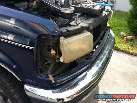 Blue Ford truck front end with headlight removed, chrome bumper, and open hood