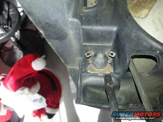 Close-up of a black plastic bracket with two screws and a central mounting point. A Santa hat is visible to the left. Text at the bottom reads 'SUPERMOTORS.NET'