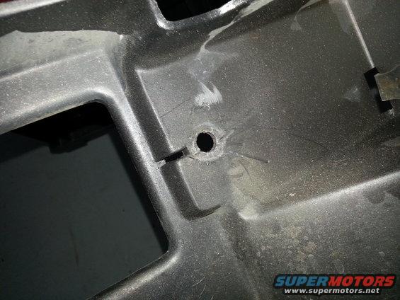Close-up of a black plastic grille section with a hole drilled in it