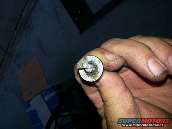 Close-up of a small, round metal part with a slot and screw, held by a dirty hand