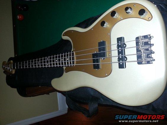 Cream-colored electric bass guitar with a gold pickguard and chrome hardware rests on a black case