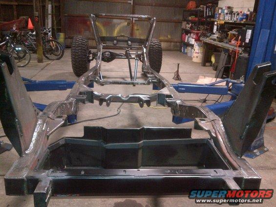 Jeep CJ frame on lift in garage, bare metal chassis with suspension and tires visible