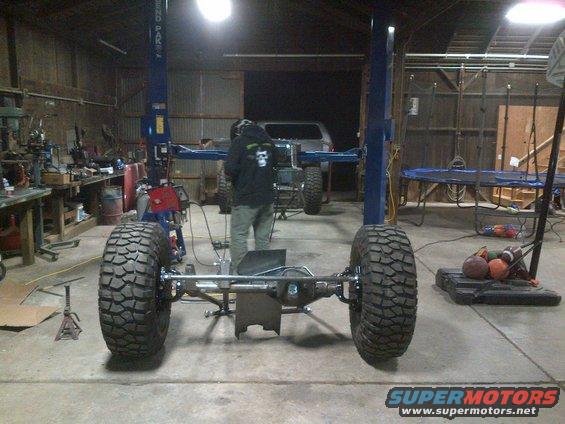 Jeep CJ chassis with large tires on a lift in a garage