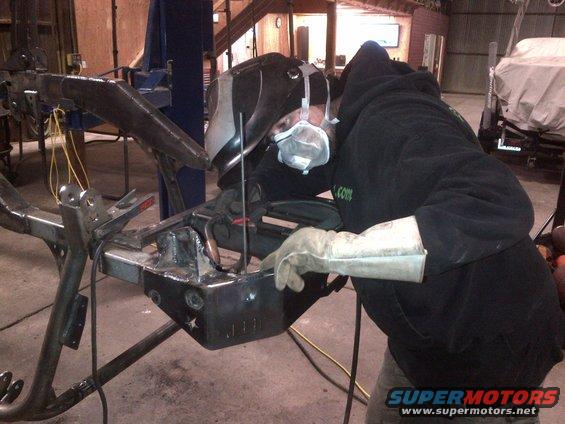 welder in mask and gloves welding metal frame in workshop
