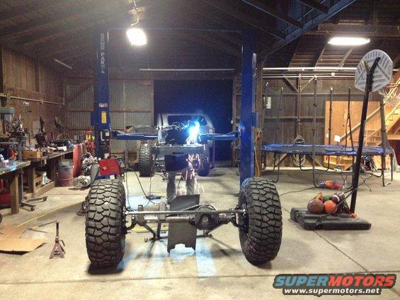 Jeep CJ frame on lift with welding sparks, large tires visible