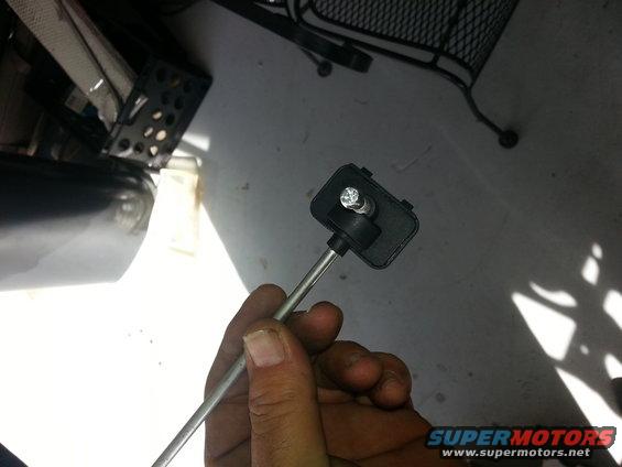 Hand holding a black plastic automotive sensor with a metal rod attached
