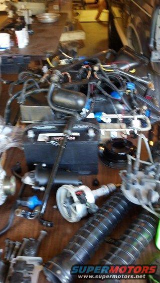 Car battery, distributor, starter, and other engine components laid out on a table