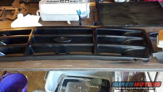 Black grille with Ford oval emblem, sitting on a workbench next to a radiator