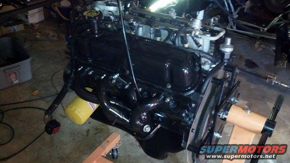 Black engine on an orange engine stand, with yellow oil filter and wiring harness