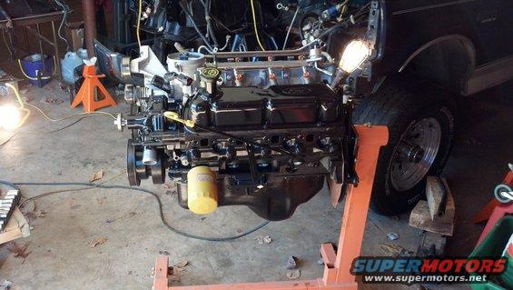 Ford V8 engine on an orange engine stand, partially installed in a vehicle. Yellow oil filter visible
