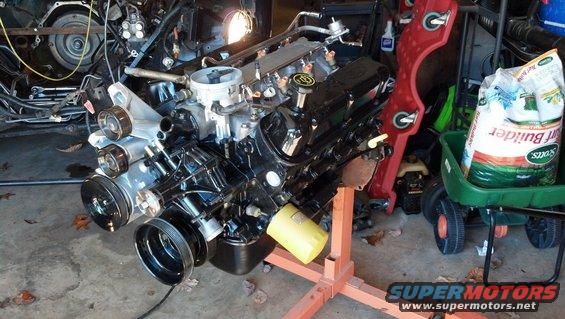 Engine on an orange stand, black with yellow oil filter. A bag of Scotts Turf Builder is in a green cart