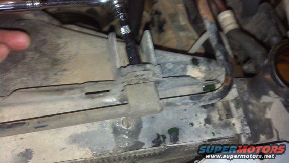Socket wrench working on a plastic fan shroud near a radiator. Green fluid is visible
