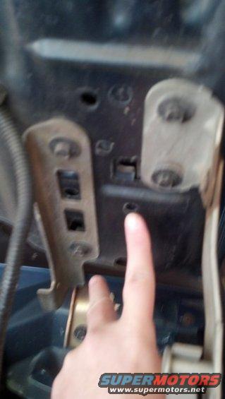 Close-up of a metal bracket and bolts in a dark engine bay, with a finger pointing