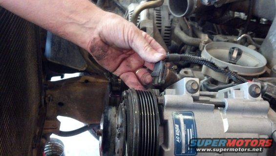 Hand disconnecting sensor in engine bay near AC compressor and radiator