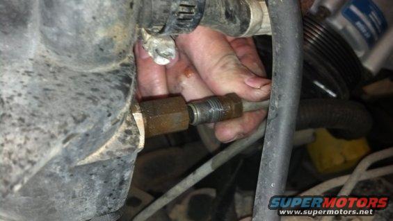 Close-up of a hand working on a metal fitting in an engine bay