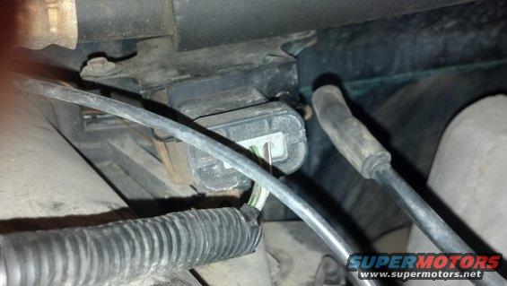 Close-up of a black electrical connector with wires attached, part of a vehicle's engine bay
