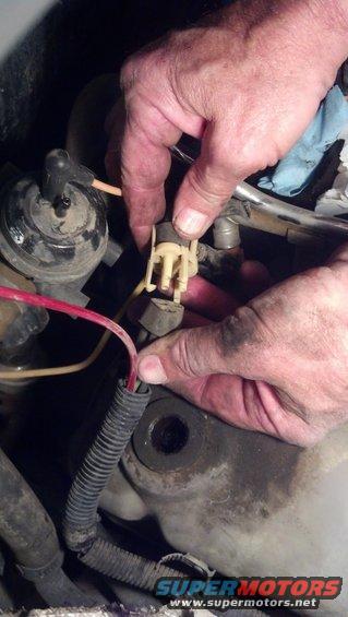 Hands disconnecting a wiring harness near engine components. A blue cloth is visible