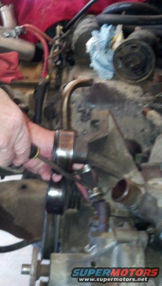 hand using a wrench on engine part, with hoses and wires visible