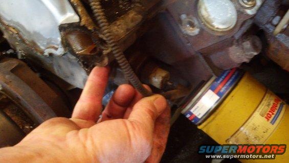 Hand touching engine component near yellow oil filter with red and blue label
