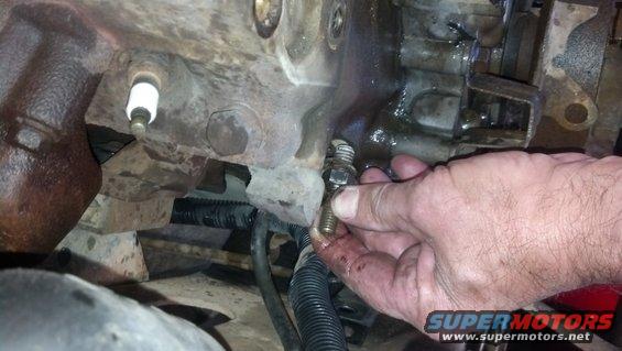 Hand removing a bolt from a greasy engine block near a spark plug